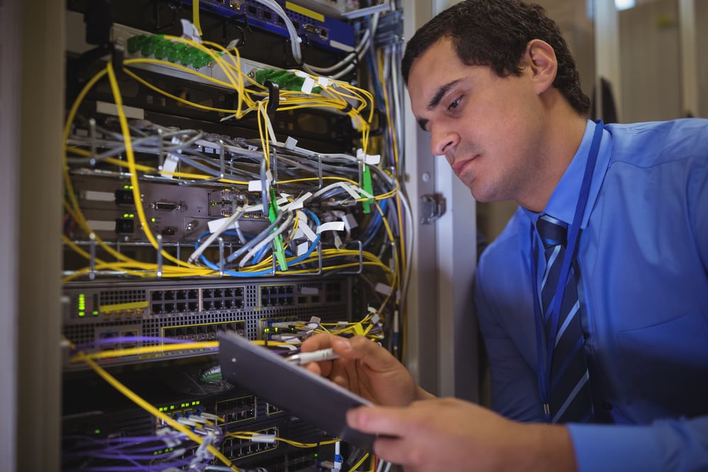 Technician maintaining record of rack mounted server on clipboard in server room